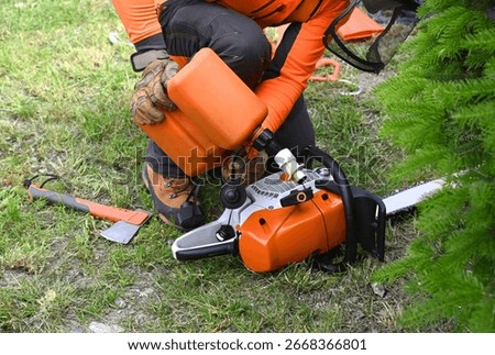 Worker adding fuel from a plastic fuel can to his chainsaw, chainsaw fueling proces