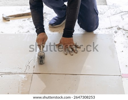 Worker adjust level tile floor with rubber mallet in the building.