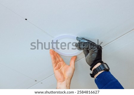 Worker adjusts circular ceiling light fixture in contemporary room, at during home improvement