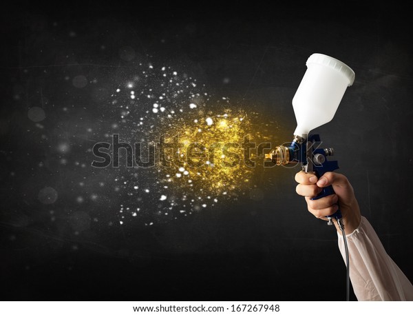 Worker with airbrush painting with glowing\
golden paint and\
particles