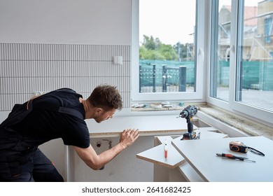 Worker aligns kitchen countertop panel in bright interior with tools. Professional furniture installation and home improvement process