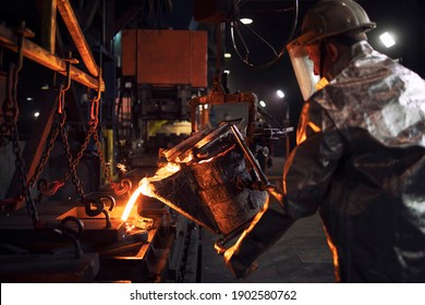 Worker in aluminized protection suit pouring molten steel in foundry. Casting metal into molds. Metallurgy and industry.