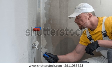 A worker applies a liquid membrane using a paint roller. Foolproof waterproofing under a tile in shower cubicle.