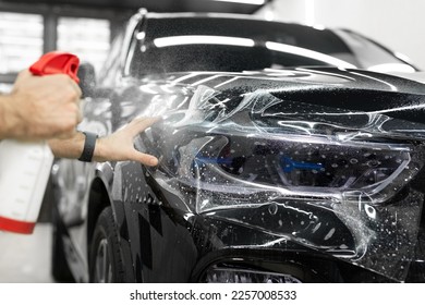 Worker applies a protective film or anti-gravity protective coating to the car headlight. Details of the car - Shutterstock ID 2257008533