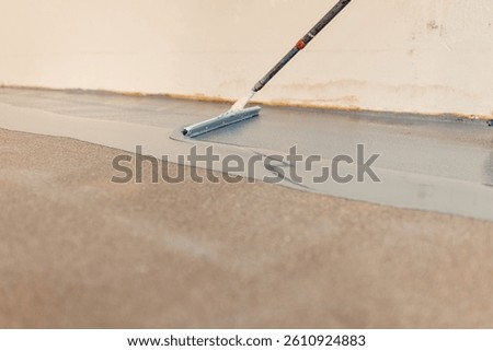 Worker applying epoxy flooring system with a notched squeegee