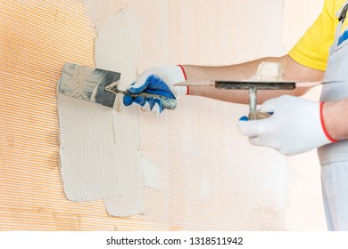 A worker is applying putty on a fiberglass mesh on the wall. He is using a trowel.