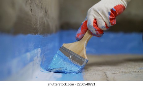 Un trabajador está aplicando pintura impermeable al suelo del baño.Aplicando una mezcla impermeable al suelo. El cuarto de baño está insonorizado por el suelo.  Trabajador que agrega recubrimiento protector y resistente al agua.