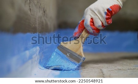 A worker is applying waterproofing paint to the floor in the bathroom.Applying a waterproofing mixture to the floor. Floor waterproofing in bathroom.  Worker adding ater resistant, protective coating.