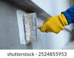 A worker is applying waterproofing paint to the wall. Applying a waterproofing mixture to the wall. Wall waterproofing on fasade. Worker adding ater resistant, protective coating.