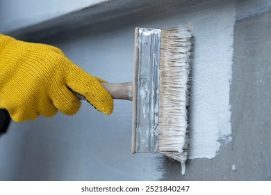 A worker is applying waterproofing paint to the wall. Applying a waterproofing mixture to the wall. Wall waterproofing on fasade. Worker adding ater resistant, protective coating.