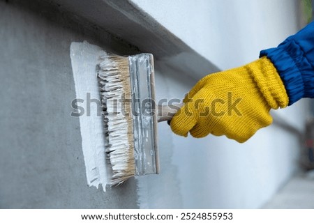A worker is applying waterproofing paint to the wall. Applying a waterproofing mixture to the wall. Wall waterproofing on fasade. Worker adding ater resistant, protective coating.