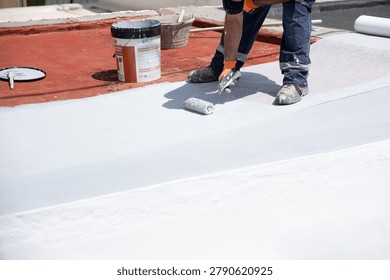 Worker applying white liquid membrane coating a roof surface for waterproofing