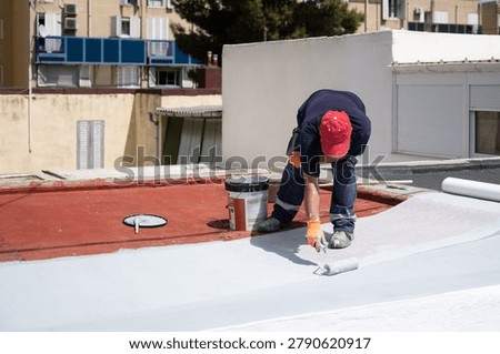 Worker applying white liquid membrane to a red roof surface using a roller