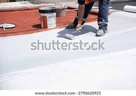 Worker applying white liquid membrane coating a roof surface for waterproofing