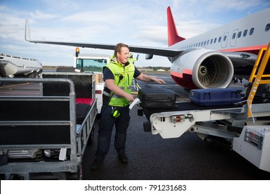 Mitarbeitende, die Gepäck auf Anhängern anfertigen, die mit dem Flugzeug verbunden sind