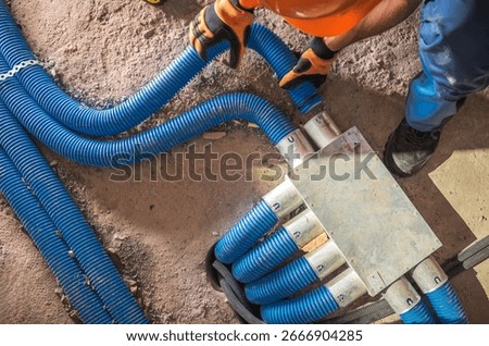 A worker assembles blue piping on the ground at a construction site, focusing intently while ensuring secure connections during daylight hours.