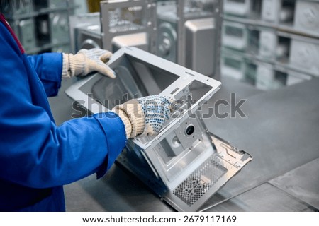 Worker assembles microwave oven casing during manufacturing process in a factory setting
