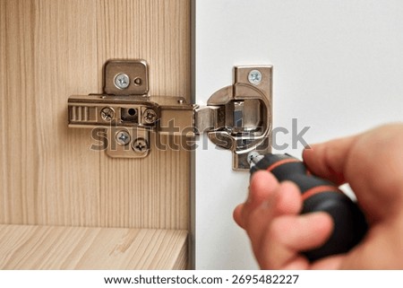 worker assembling cabinet and screwing door hinge at home, close-up