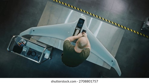 Worker Assembling Drones For National Security. Adult Man in Camouflage Engaged in Specialized Assembly of Large, High tech Drone on Metal Workbench. Future of National Security Production. Top View.