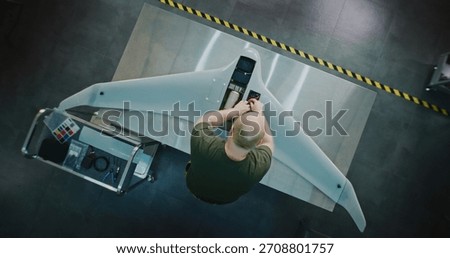 Worker Assembling Drones For National Security. Adult Man in Camouflage Engaged in Specialized Assembly of Large, High tech Drone on Metal Workbench. Future of National Security Production. Top View.