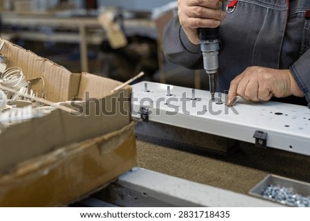 Worker assembling white metal panel with power drill in workshop