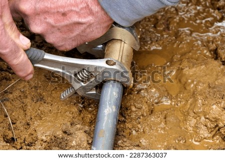Worker attaching brass joint connector to old and new water pipes using adjustable spanners
