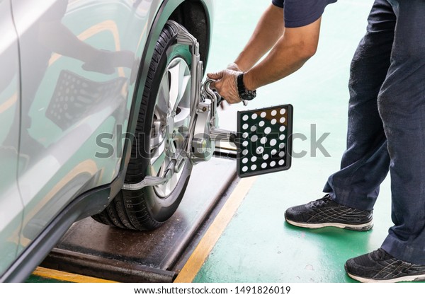 Worker attaching wheel alignment device\
equipment onto wheel car in workshop\
garage