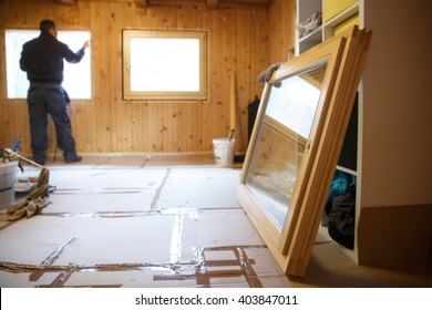 Worker in the background installing new, three pane wooden windows in an old wooden house, with a new window in the foreground. Home renovation, sustainable living, energy efficiency concept. 