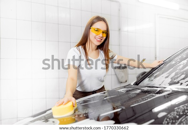 Worker beautiful woman cleaning auto\
black foam with yellow sponge. Car washing\
service.