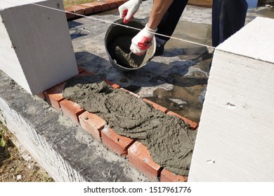 The worker begins the first row of masonry construction in white gas blocks. - Shutterstock ID 1517961776