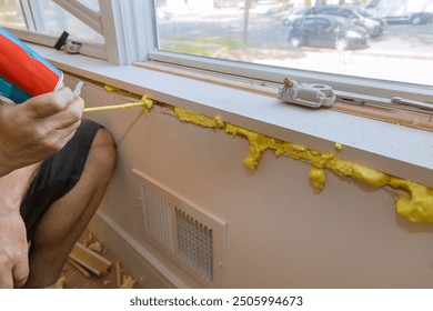 Worker blows construction foam into gap between window wall