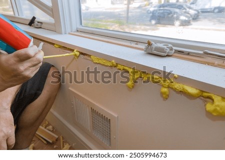 Worker blows construction foam into gap between window wall