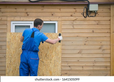 a worker in a blue uniform, blocks the window of the house with a protective shield made of wood, from thieves, when moving to another address, there is a place for the inscription