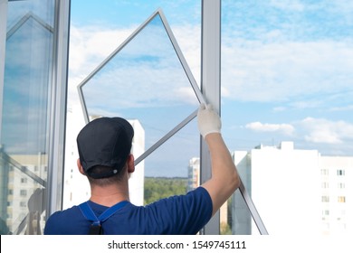 a worker in a blue uniform, rear view, installs a mosquito net in a plastic window frame, against the sky