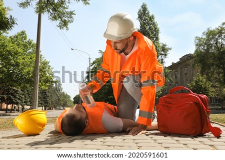 Worker with bottle of water helping colleague on city street. Suffering from heat stroke