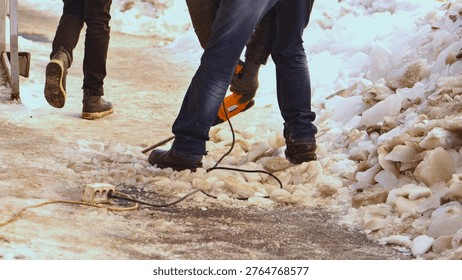 Worker breaking up thick ice using a jackhammer on a sidewalk during winter