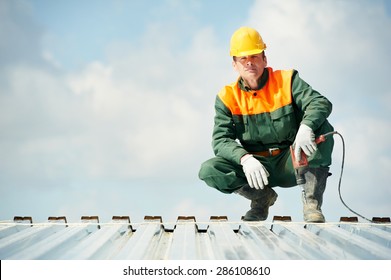 worker builder with hand drill at metal profile roof installation