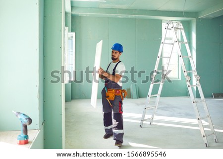 Worker builder installs plasterboard drywall at a construction