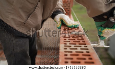 Worker builds a wall of colored brick. Worker in Close up of industrial bricklayer installing bricks and mortar cement brick on construction site