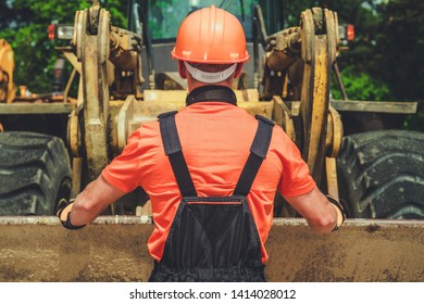 Worker And The Bulldozer. Caucasian Heavy Duty Equipment Operator In His 30s In Front Of The Machine.