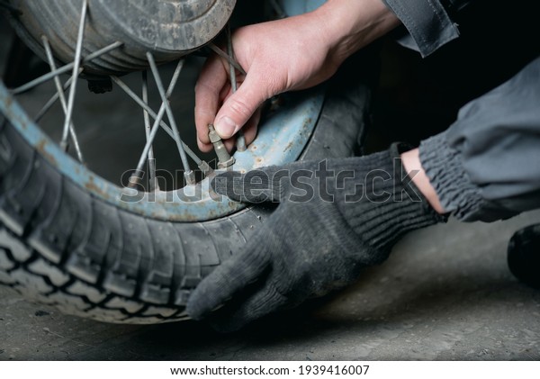 A worker of car fitting service unscrews a cap\
from a motorbike wheel close\
up.