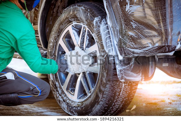 Worker in car wash shop under\
working to clean customer car wheels by soap form,car service\
concept.