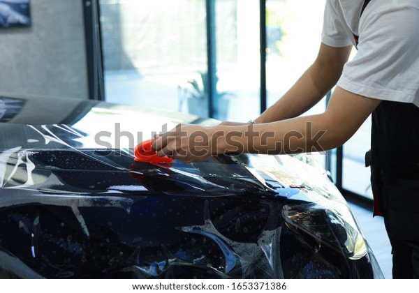 worker Car wrapping film in the\
Car  shop. Car wrapping specialist putting vinyl foil or film on\
car
