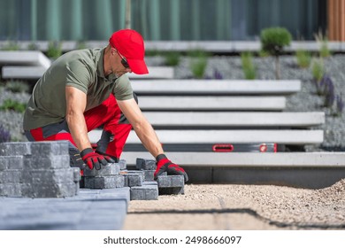 A worker is carefully placing pavers in a contemporary outdoor space while wearing safety gloves and sunglasses. - Powered by Shutterstock