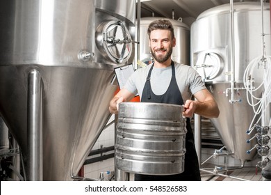 Worker carrying barrel with beer at the brewery with metal containers on the background - Powered by Shutterstock