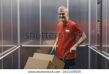 Worker carrying boxes in the elevator using a hand truck, he is smiling at camera, delivery and relocation concept