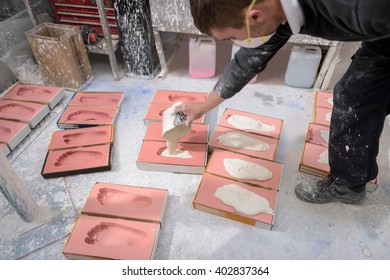 Worker casting plaster into foot moulds for orthopaedic support in factory