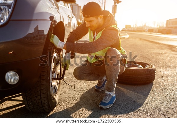 Worker changes a broken
wheel of a car. The driver should replace the old wheel with a
spare. Man changing wheel after a car breakdown. Transportation,
traveling concept