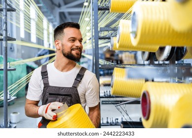 Worker changing thread spool on industrial knitting machine inside textile factory.