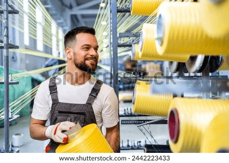 Worker changing thread spool on industrial knitting machine inside textile factory.